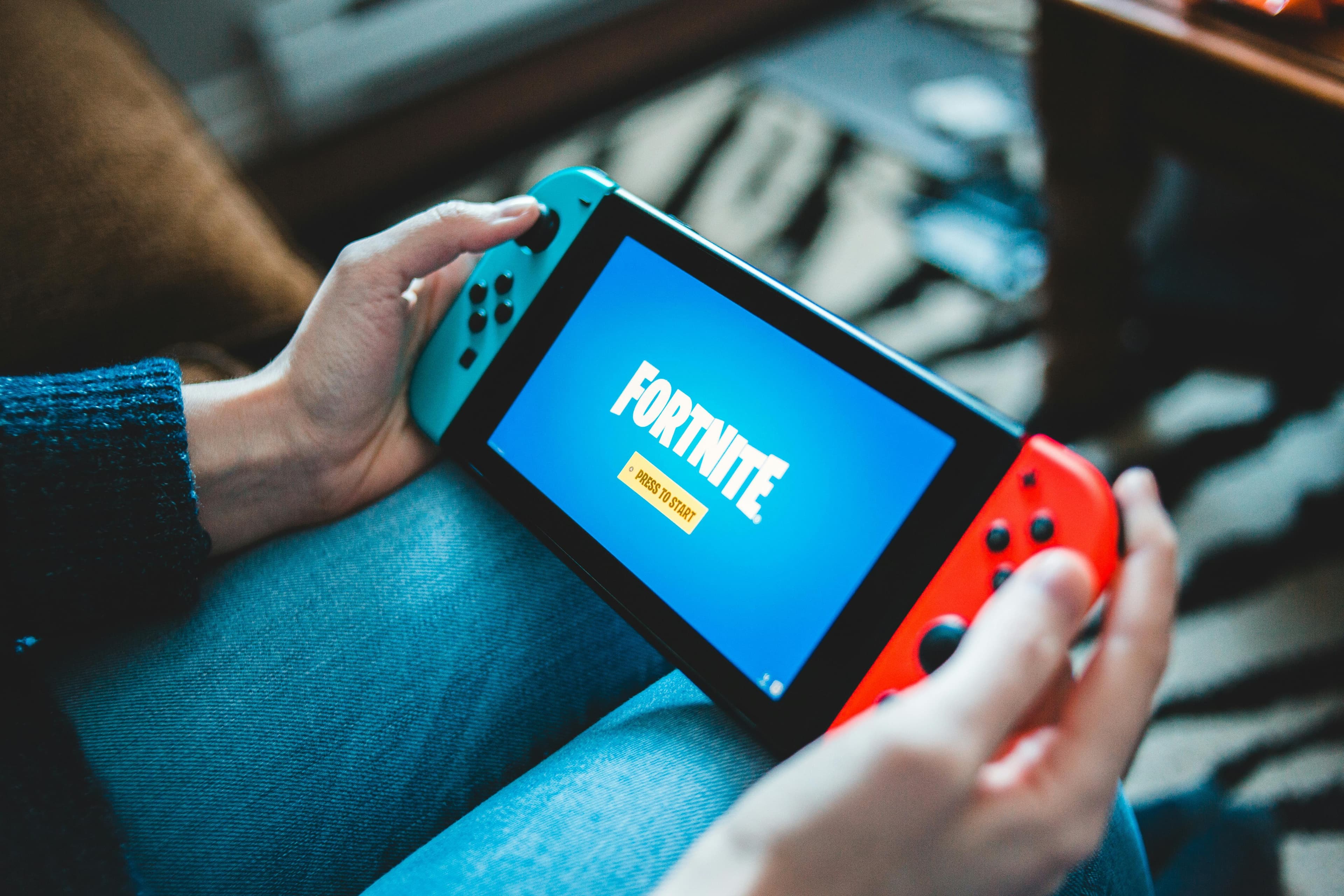 Hender som holder en rød og blå Nintendo Switch. Fortnite logoen vises på skjermen.